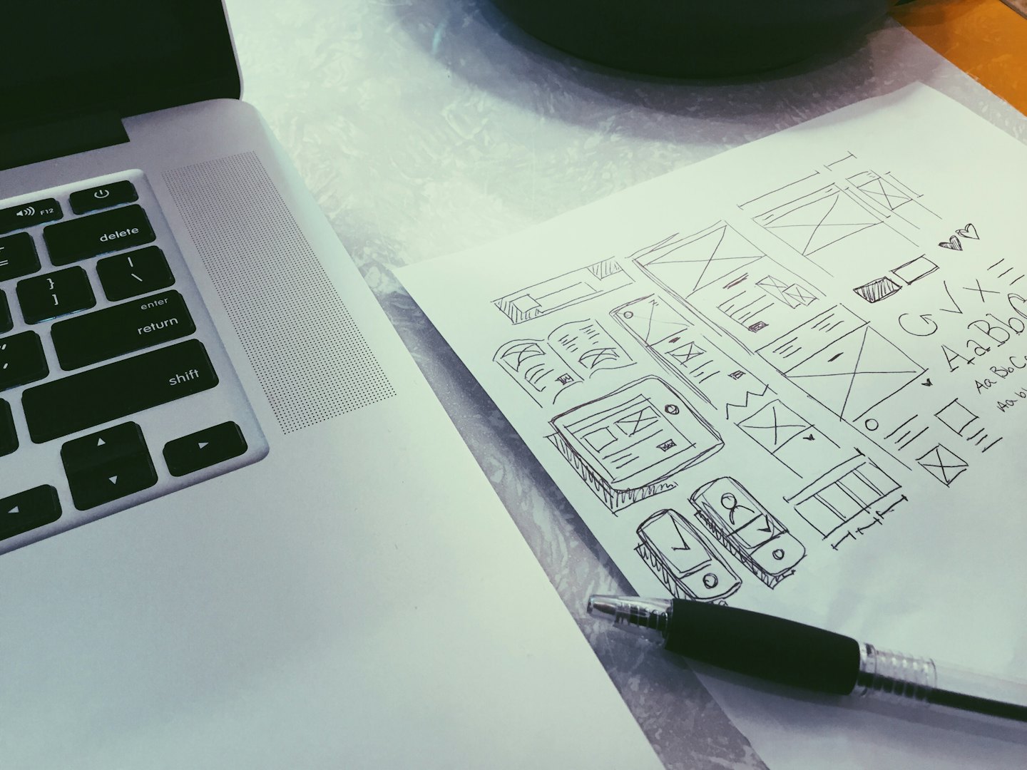 Laptop toetsenbord met pen en papieren wireframe schetsen.